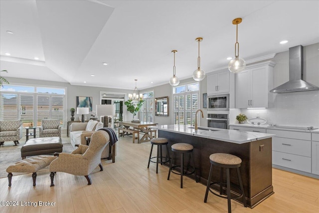 kitchen featuring an island with sink, wall chimney exhaust hood, light wood-type flooring, and a wealth of natural light