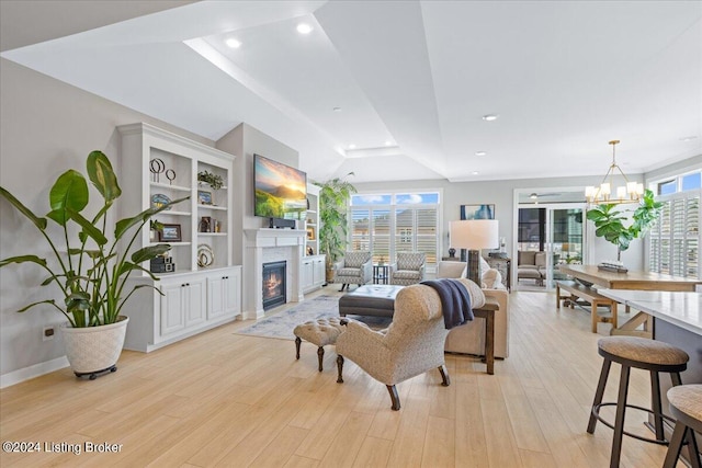 living room featuring light hardwood / wood-style flooring, a premium fireplace, a raised ceiling, and an inviting chandelier