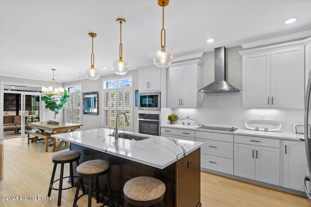 kitchen featuring a kitchen island with sink, sink, wall chimney exhaust hood, light hardwood / wood-style flooring, and appliances with stainless steel finishes