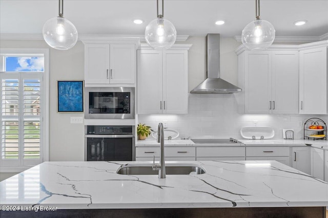 kitchen with appliances with stainless steel finishes, hanging light fixtures, wall chimney exhaust hood, and sink