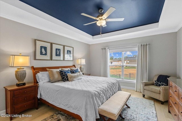 bedroom featuring light hardwood / wood-style flooring, a tray ceiling, ceiling fan, and crown molding