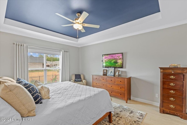 bedroom featuring light wood-type flooring, a raised ceiling, ornamental molding, and ceiling fan