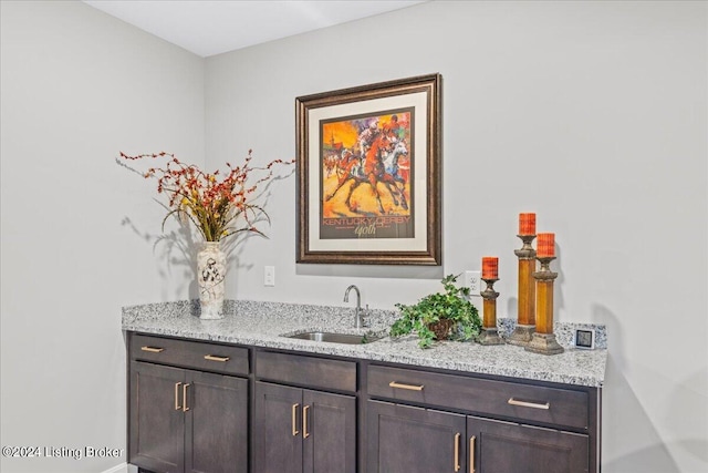 bar with dark brown cabinetry, light stone counters, and sink