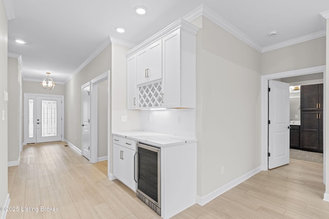 kitchen with white cabinetry, wine cooler, ornamental molding, light stone countertops, and light wood-type flooring