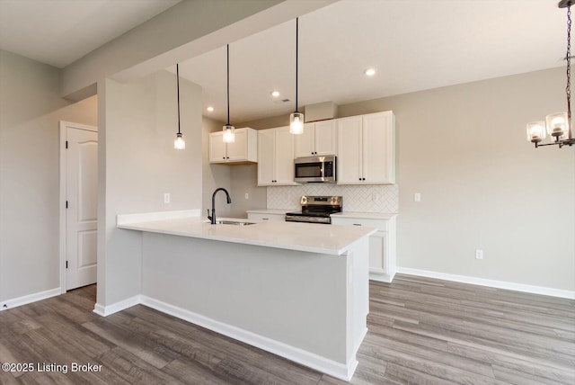 kitchen with appliances with stainless steel finishes, a sink, wood finished floors, light countertops, and decorative backsplash