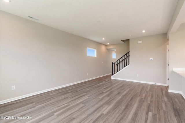 unfurnished room with wood finished floors, stairs, recessed lighting, and baseboards