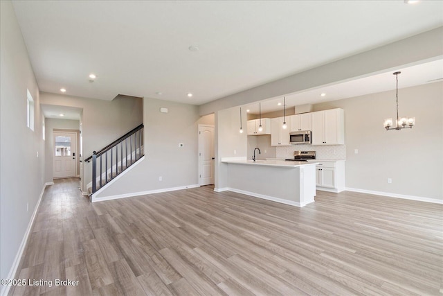 unfurnished living room featuring light wood-style flooring, recessed lighting, stairway, baseboards, and a chandelier