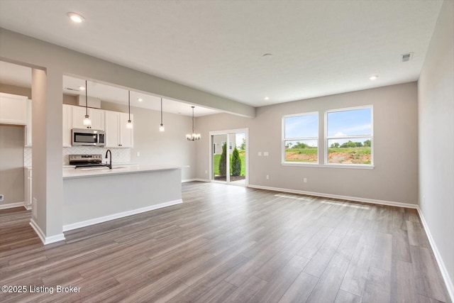 unfurnished living room featuring wood finished floors, baseboards, recessed lighting, and a chandelier
