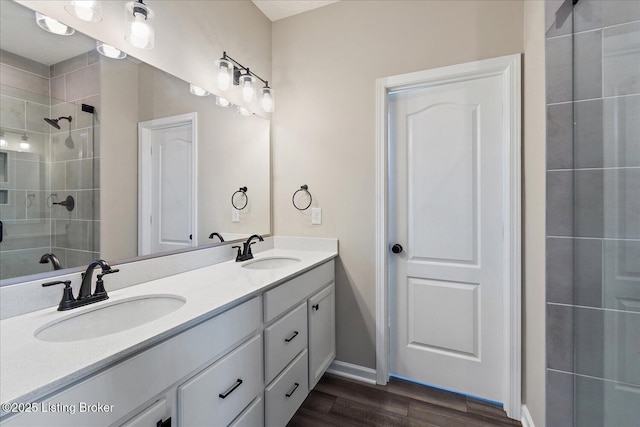 bathroom featuring a tile shower, double vanity, baseboards, and wood finished floors