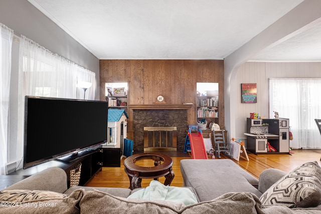 living room with ornamental molding, wood walls, a stone fireplace, and hardwood / wood-style flooring