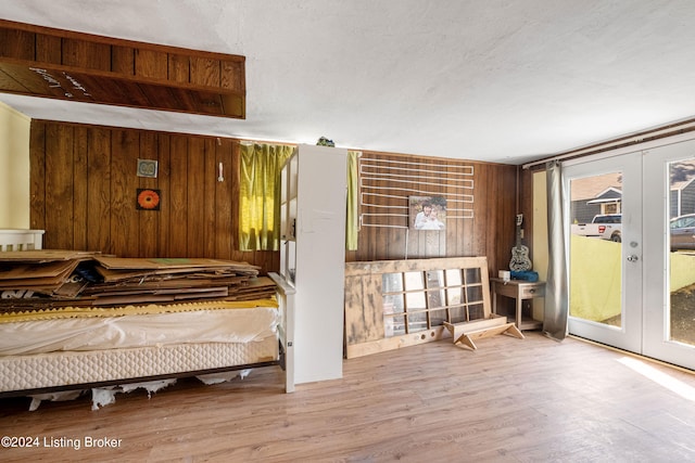 bedroom with a textured ceiling, light hardwood / wood-style flooring, wood walls, and french doors