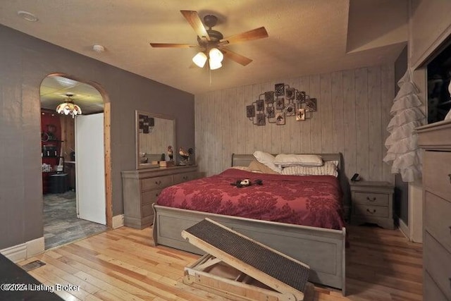 bedroom with ceiling fan, wooden walls, and hardwood / wood-style flooring