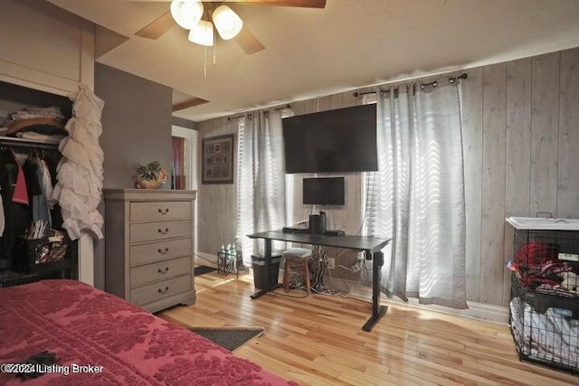 bedroom with light wood-type flooring, wood walls, and ceiling fan