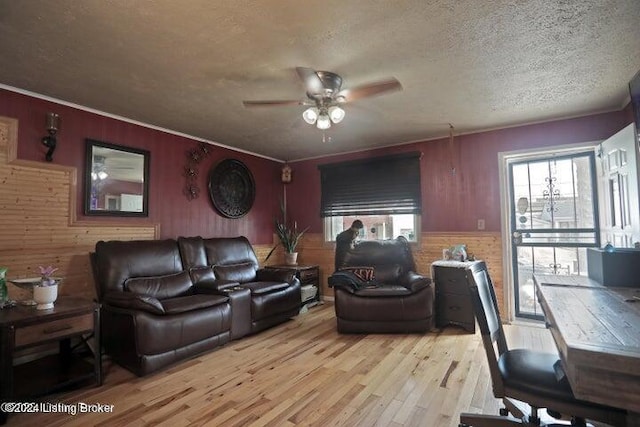 living room with a textured ceiling, ceiling fan, wooden walls, and light hardwood / wood-style floors