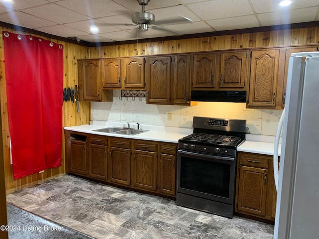 kitchen featuring white refrigerator, sink, a drop ceiling, ceiling fan, and stainless steel range with gas cooktop