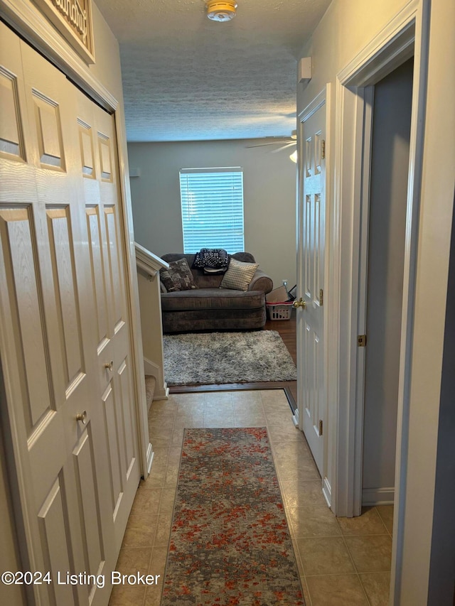 corridor with a textured ceiling and light tile patterned flooring