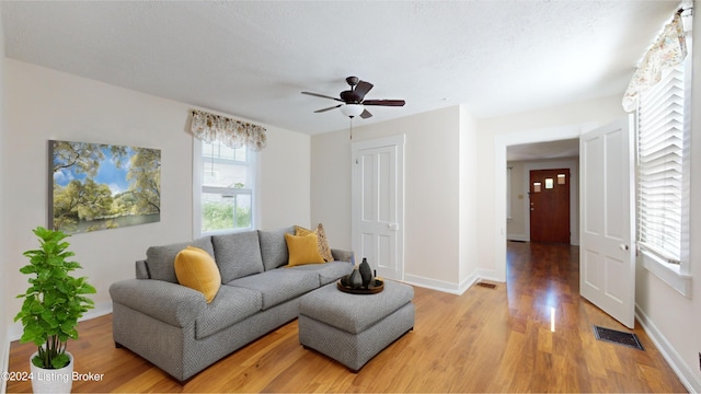 living room featuring ceiling fan, light hardwood / wood-style floors, and a textured ceiling