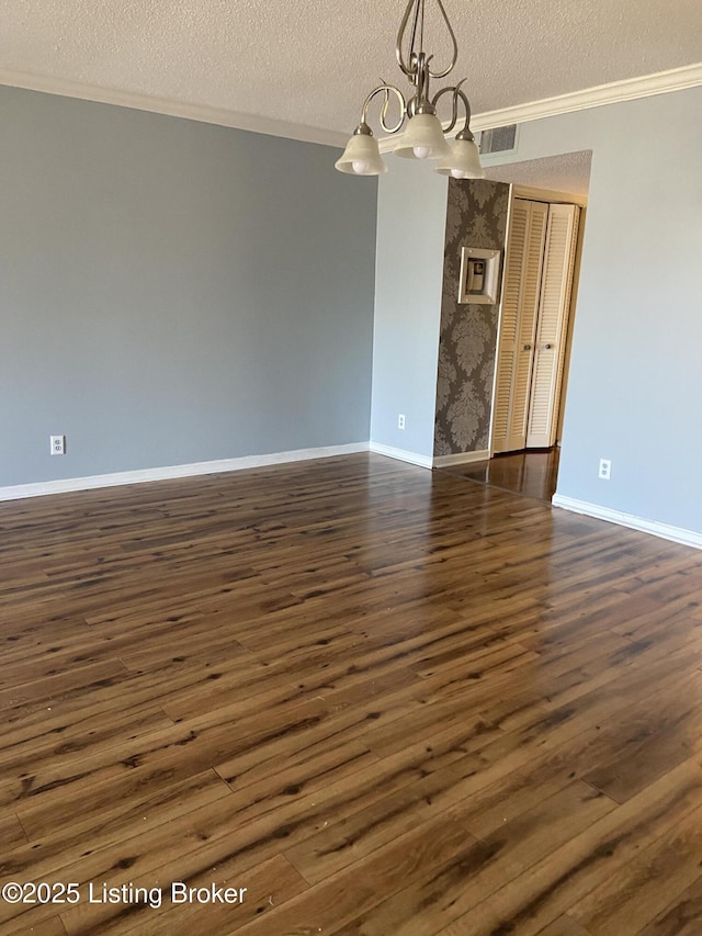 unfurnished room featuring dark wood-type flooring, ornamental molding, a textured ceiling, and a notable chandelier