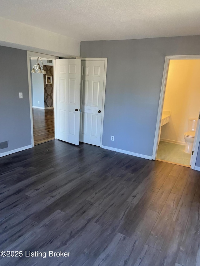 unfurnished bedroom with ensuite bath, dark hardwood / wood-style flooring, a closet, and a textured ceiling