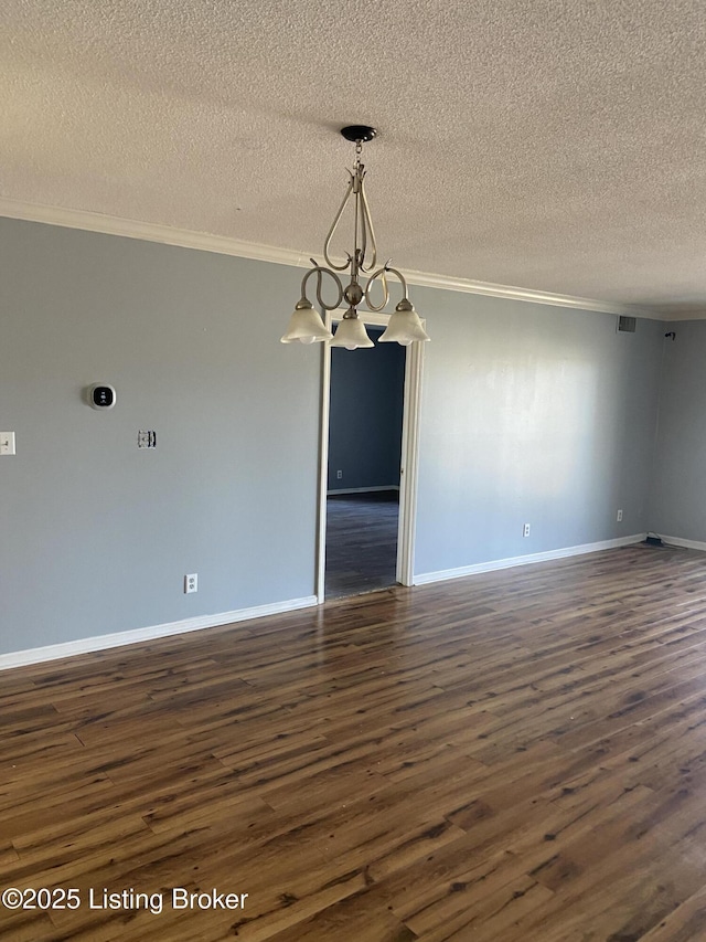 empty room featuring dark hardwood / wood-style flooring, ornamental molding, a textured ceiling, and an inviting chandelier