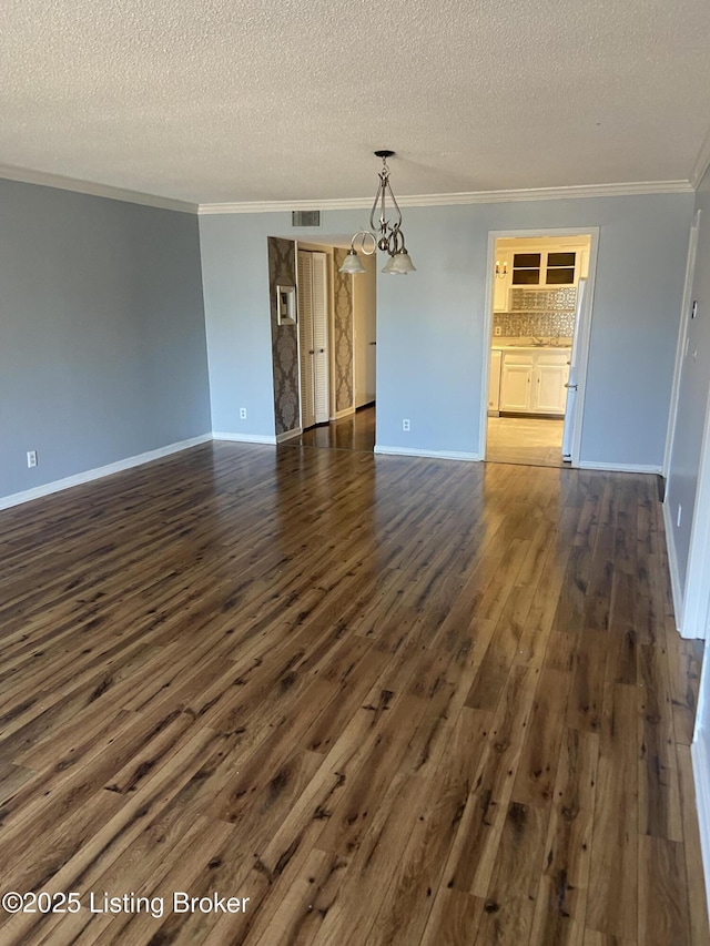 spare room with a notable chandelier, crown molding, dark wood-type flooring, and a textured ceiling