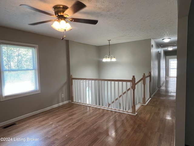 unfurnished room featuring ceiling fan with notable chandelier, a textured ceiling, and dark hardwood / wood-style floors