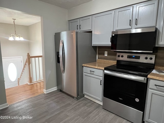 kitchen featuring stainless steel appliances, light wood-type flooring, a textured ceiling, decorative light fixtures, and a notable chandelier