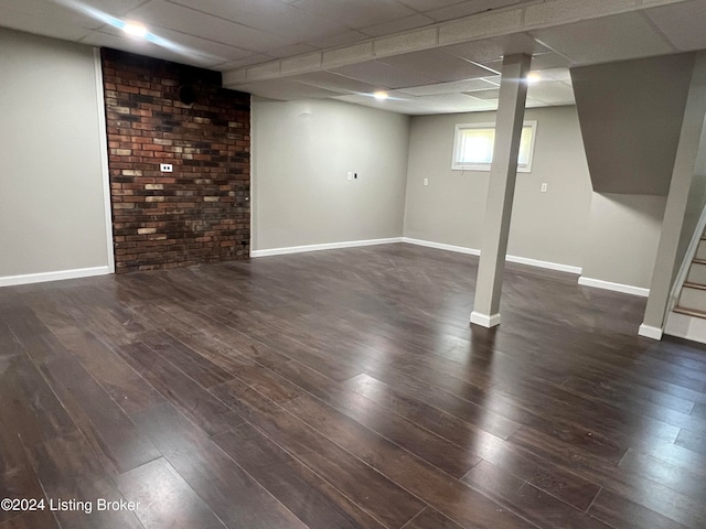 basement featuring brick wall, dark hardwood / wood-style floors, and a paneled ceiling