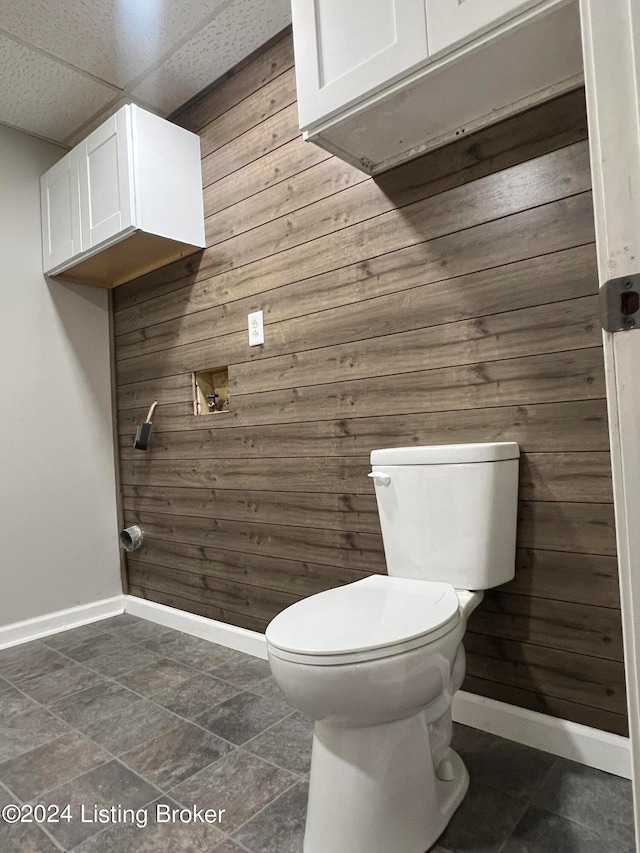 bathroom with a drop ceiling, wooden walls, and toilet