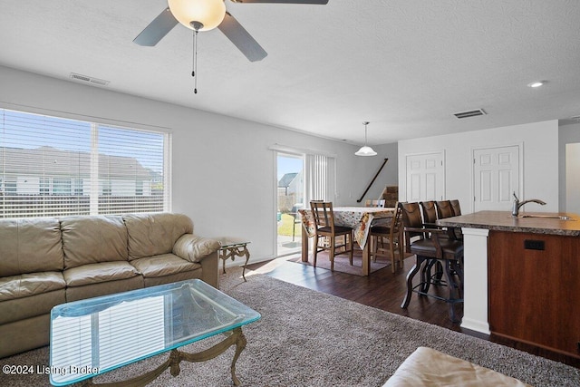 living room featuring ceiling fan, sink, plenty of natural light, and dark wood-type flooring