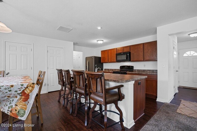 kitchen with a kitchen breakfast bar, black appliances, a kitchen island with sink, and dark hardwood / wood-style flooring