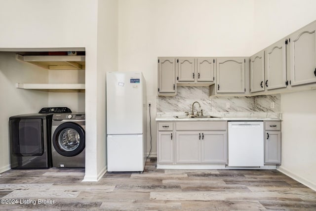 kitchen featuring tasteful backsplash, sink, washing machine and clothes dryer, light hardwood / wood-style flooring, and white appliances