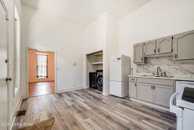 kitchen featuring sink, white appliances, high vaulted ceiling, separate washer and dryer, and light hardwood / wood-style floors