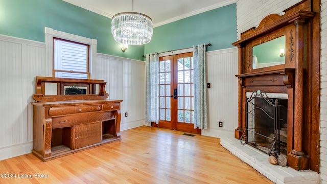 interior space featuring a brick fireplace, ornamental molding, light wood-type flooring, and french doors