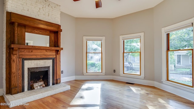 unfurnished living room with a wealth of natural light, light hardwood / wood-style floors, ceiling fan, and a large fireplace