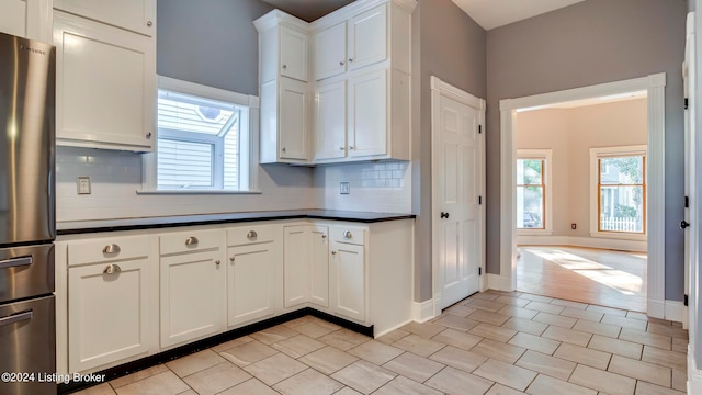 kitchen featuring stainless steel refrigerator, backsplash, white cabinetry, and a wealth of natural light