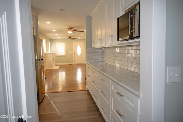 kitchen featuring stainless steel refrigerator, white cabinetry, light hardwood / wood-style floors, and light stone counters