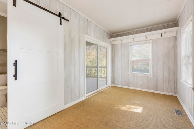 spare room with a barn door, wood walls, crown molding, and light carpet