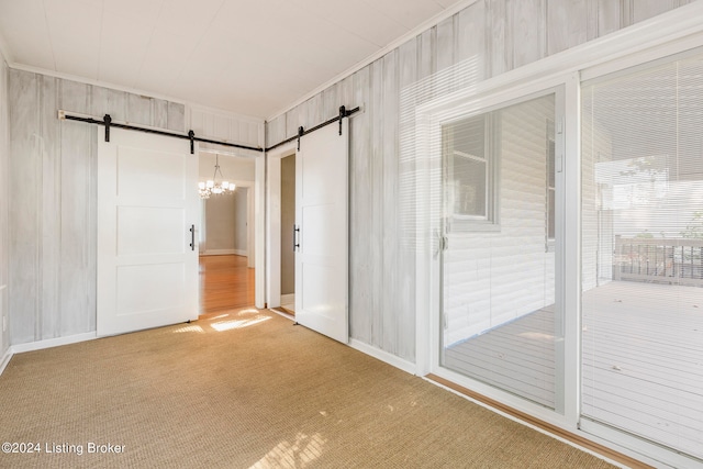 carpeted spare room featuring ornamental molding, wooden walls, and a barn door