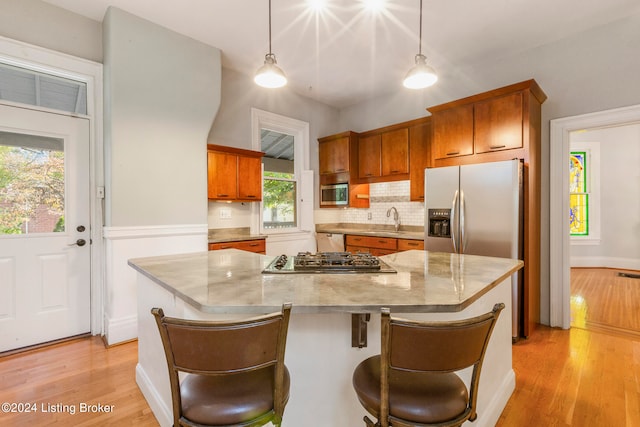 kitchen featuring appliances with stainless steel finishes, light wood-type flooring, decorative light fixtures, and a center island