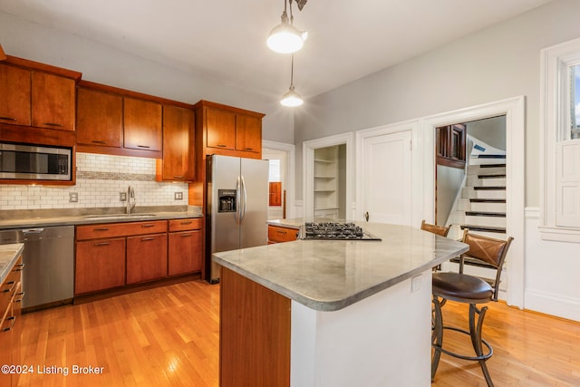 kitchen with sink, a kitchen island, decorative light fixtures, appliances with stainless steel finishes, and light wood-type flooring