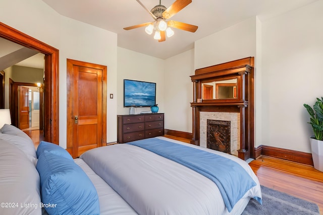 bedroom featuring a fireplace, light wood-type flooring, and ceiling fan