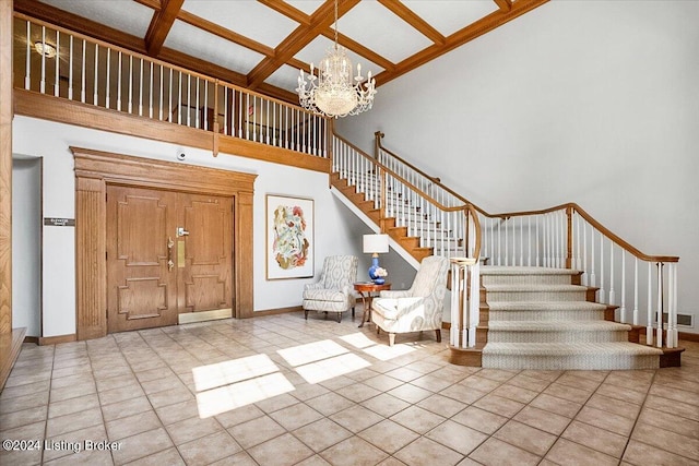 foyer with coffered ceiling, a towering ceiling, light tile patterned floors, and a chandelier