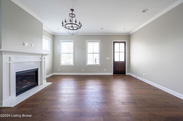 unfurnished living room with an inviting chandelier, plenty of natural light, dark wood-type flooring, and crown molding