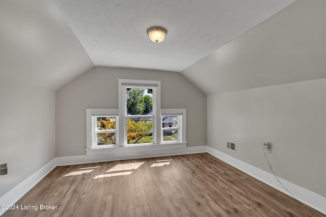 additional living space with wood-type flooring, lofted ceiling, and a textured ceiling