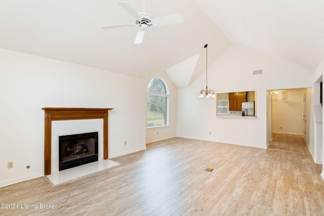 unfurnished living room featuring ceiling fan with notable chandelier, light hardwood / wood-style floors, a tiled fireplace, and high vaulted ceiling