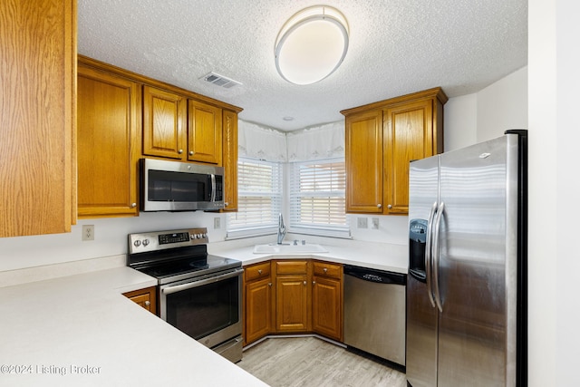 kitchen featuring a textured ceiling, light wood-type flooring, sink, and stainless steel appliances