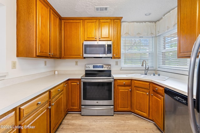 kitchen featuring a textured ceiling, sink, light hardwood / wood-style flooring, and stainless steel appliances