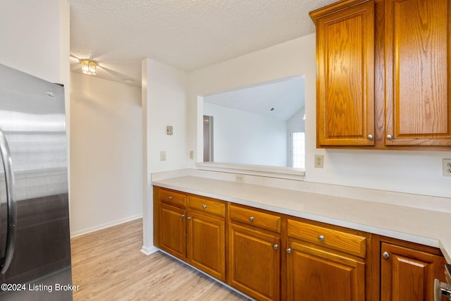 kitchen featuring light wood-type flooring, stainless steel refrigerator, and a textured ceiling