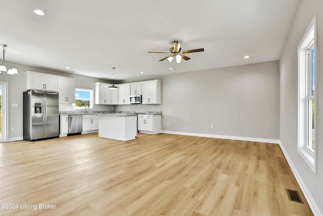 kitchen featuring appliances with stainless steel finishes, white cabinetry, ceiling fan with notable chandelier, pendant lighting, and light hardwood / wood-style flooring